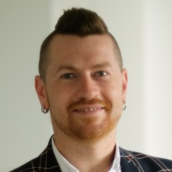 Smiling person wearing white shirt and blue jacket with dark red stripes